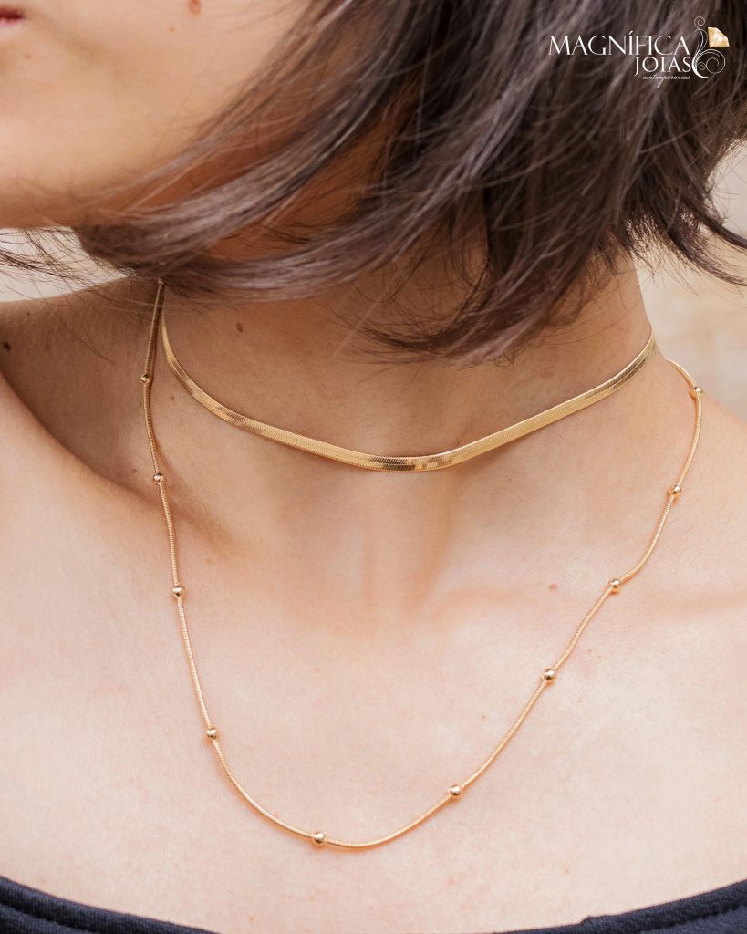 modelo usando choker dourado e liso e colar longo de bolinhas em um mi de colar semijoia